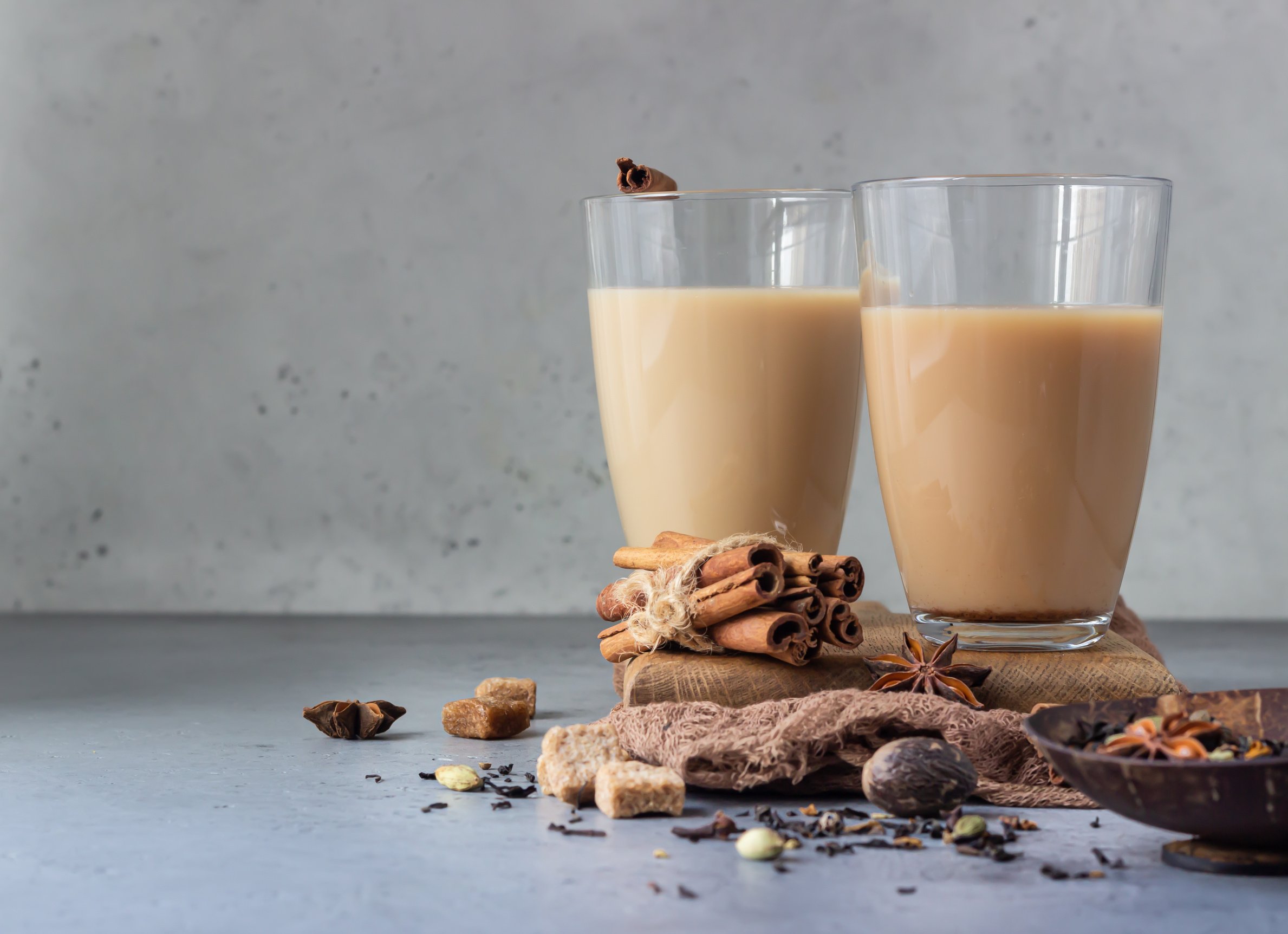 Traditional Indian drink - masala chai tea (milk tea) with spices in drinking glasses on grey stone background with spices for making tea.